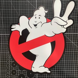 May include: A white ghost character with a smiling expression making a peace sign with one hand, positioned in front of a red circular prohibition symbol with a diagonal slash, rendered in a flat graphic style with bold black outlines.