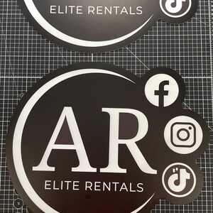 May include: Two circular black signs with white text reading AR ELITE RENTALS. The signs feature white social media icons for Facebook, Instagram, and TikTok on the right side. A white curved line frames the text within the circular design.