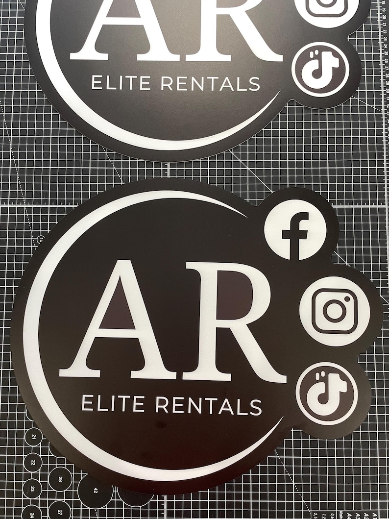 May include: Two circular black signs with white text reading AR ELITE RENTALS. The signs feature white social media icons for Facebook, Instagram, and TikTok on the right side. A white curved line frames the text within the circular design.