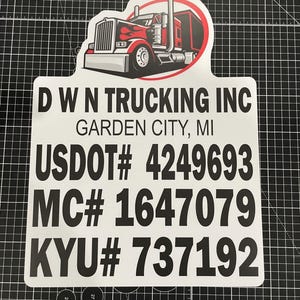 May include: A white rectangular sign with rounded top corners featuring a red and black semi-truck graphic. The text reads D W N TRUCKING INC, GARDEN CITY, MI, USDOT# 4249693, MC# 1647079, and KYU# 737192 in bold black lettering on a white background.