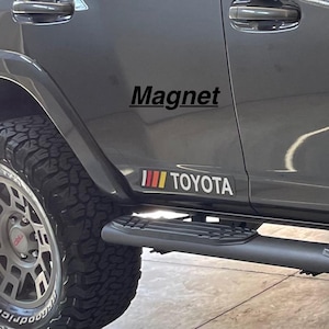 May include: A gray Toyota SUV with a black "Magnet" decal and a red, yellow, and white stripe decal with the word "TOYOTA" on the side.