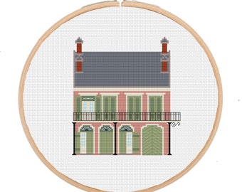May include: Cross stitch pattern of a pink and green New Orleans style house with a balcony and black railings. The house has a gray roof and two chimneys.