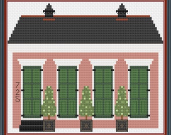 May include: A pink house with four green windows and shutters, a black roof, and two white chimneys. There are three green trees in front of the house, each in a black pot with a star design. The house has a black door and the number "721" is written on the side.