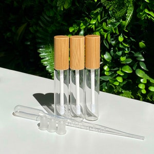 May include: Three clear glass bottles with bamboo lids and white applicators. The bottles are on a white surface with three clear plastic droppers and three clear plastic caps.