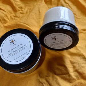 May include: Two white jars with black lids and labels. The labels have a black and yellow logo and the text "Tallow Talk", "Citrus + Tea", and "Tree Deodorant".
