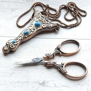 May include: A vintage-style copper sewing kit and matching scissors. The kit has turquoise-coloured stones and decorative scrollwork. The scissors have leaf-shaped details.