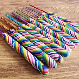 May include: A set of nine crochet hooks with colourful, swirled polymer clay handles and metallic tips. Each hook features a size marking ranging from 2.0mm to 6.5mm printed on the metal shaft. The handles display a vibrant, multi-coloured striped pattern.