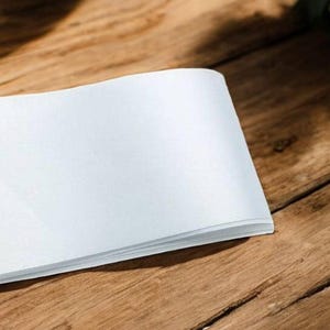 May include: A white blank book lying closed on a wooden surface.