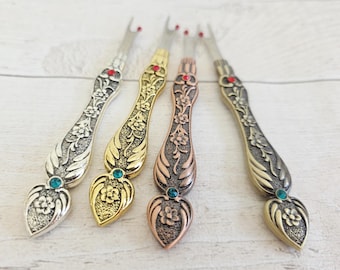 May include: Four decorative seam rippers with ornate floral designs. Each ripper features a different metallic finish: silver, gold, copper, and bronze. They have jewel accents in red and teal, and are ideal for sewing and crafting.