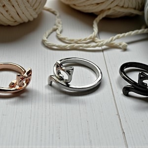 Könnte beinhalten: Drei Metallringe in einer Reihe, jeder mit einem stilisierten Katzendesign. Der erste Ring ist roségold, der zweite silberfarben und der dritte schwarz. Jeder Ring hat eine Ringschiene, die sich zu Katzenohren und einem Schwanz formt.