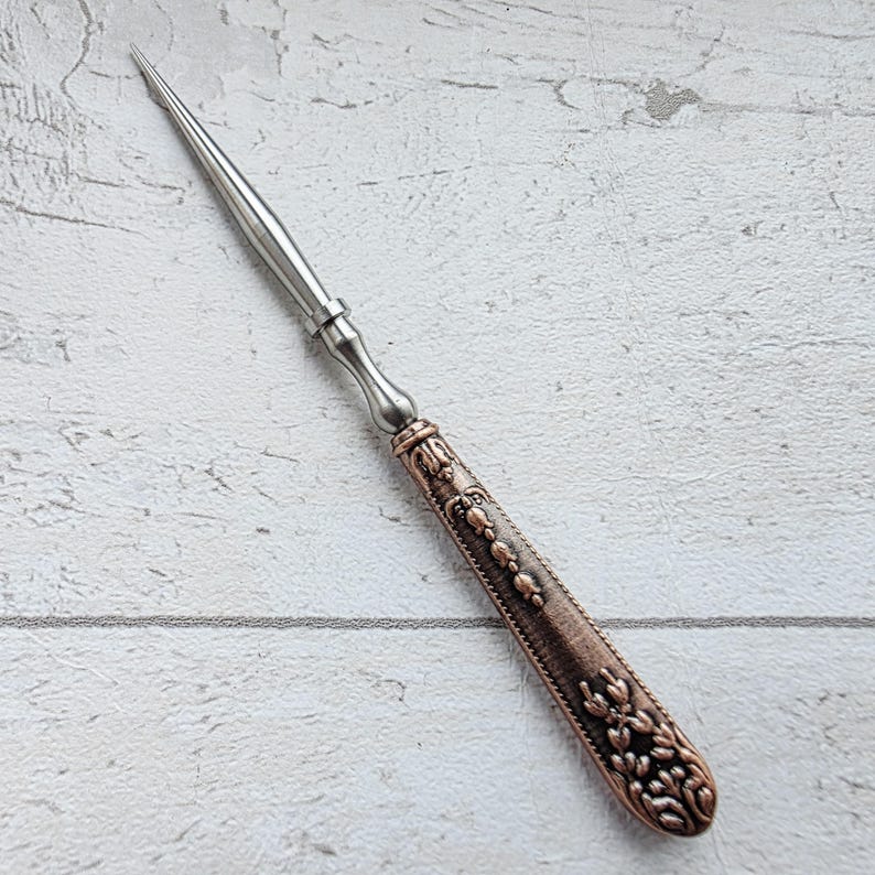 May include: A letter opener with a silver blade and a decorative handle. The handle is a copper color with floral and beaded designs. The letter opener is approximately 8 inches long.