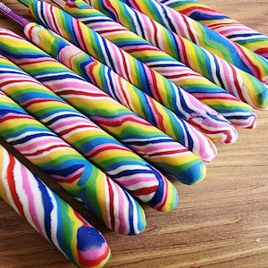 May include: A collection of crochet hooks featuring thick, custom-moulded handles with a vibrant, multi-coloured swirl pattern of red, yellow, green, blue, and pink. The metal hook tips are visible, with some showing size markings like 5.0mm.