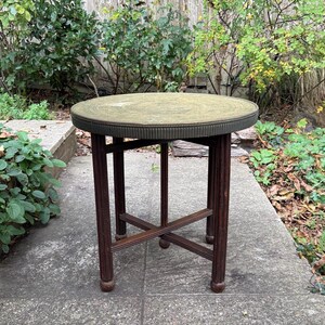 May include: A small, round side table with a dark brown wooden frame. The tabletop is a light green colour with a decorative edge. The table is approximately 61 cm tall and 51 cm in diameter.