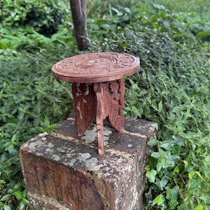 May include: A small, intricately carved wooden table with a round top and three legs. The table is made of reddish-brown wood and features detailed floral patterns on the tabletop and legs. It is approximately 30 cm in diameter.