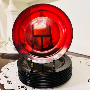 May include: A stack of 10 black glass plates with a single red glass plate on top. The red plate has a raised rim and a shiny finish.