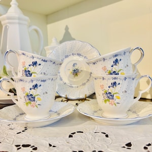 May include: A white porcelain tea set with blue floral designs and a blue dotted pattern. The set includes teacups, saucers, and a serving plate. The teacups have curved handles and the rims are trimmed in blue.