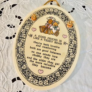 May include: A white ceramic plaque with a floral border and a message about friendship. The plaque features two teddy bears hugging and the text "A good friend is like a teddy bear they're both lovable and comforting both are good listeners no one minds how chubby they are and the older they get the more valuable they become."