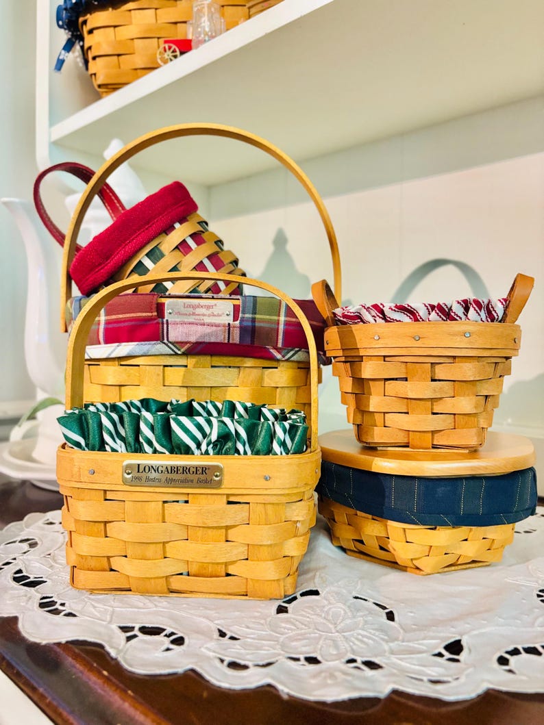 May include: A collection of Longaberger baskets in various sizes and shapes. The baskets are made of woven wood and feature fabric liners in red, green, and blue plaid patterns. Some baskets have handles, and one has a metal tag that reads "Longaberger".