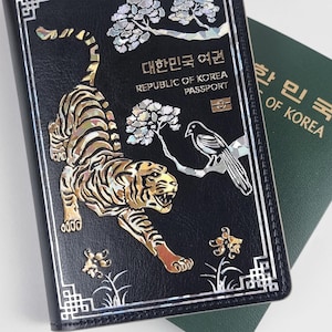 May include: Black passport cover with a tiger and bird design. The cover features the text "REPUBLIC OF KOREA PASSPORT" in English and Korean. The tiger and bird are inlaid with a shimmering, iridescent material.