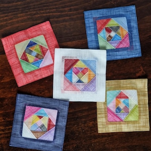 Peut inclure: Cinq dessous-de-verre en tissu colorés avec un motif géométrique. Chaque dessous-de-verre est fait d'un tissu différent avec un fond de couleur différent. Les dessous-de-verre sont disposés en rangée sur une surface en bois.