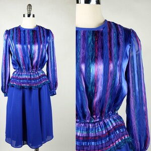 Peut inclure: Une robe à rayures bleues et violettes avec une taille froncée et des manches longues. La robe a une jupe bleue et un corsage à rayures violettes, bleues et vertes.