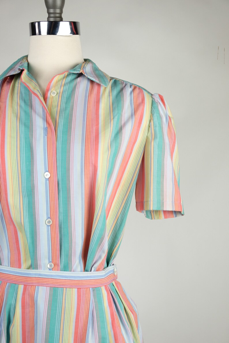 May include: A striped dress with a button-up front and short sleeves. The dress is made of a light fabric and has a variety of colors, including pink, blue, green, and yellow.