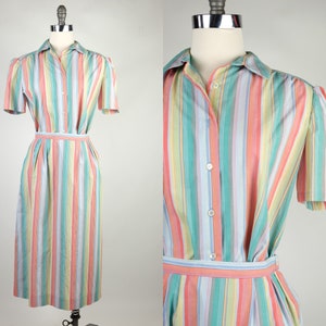 May include: A striped dress with a button-up front and short sleeves. The dress has a light blue, pink, green, and yellow striped pattern. The dress has a belt.