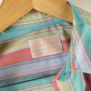 May include: A striped button-down shirt with a light blue, yellow, green, and pink color scheme. The shirt has a label that reads "Country Sophisticates, Portland, Oregon, a division of Pendleton."