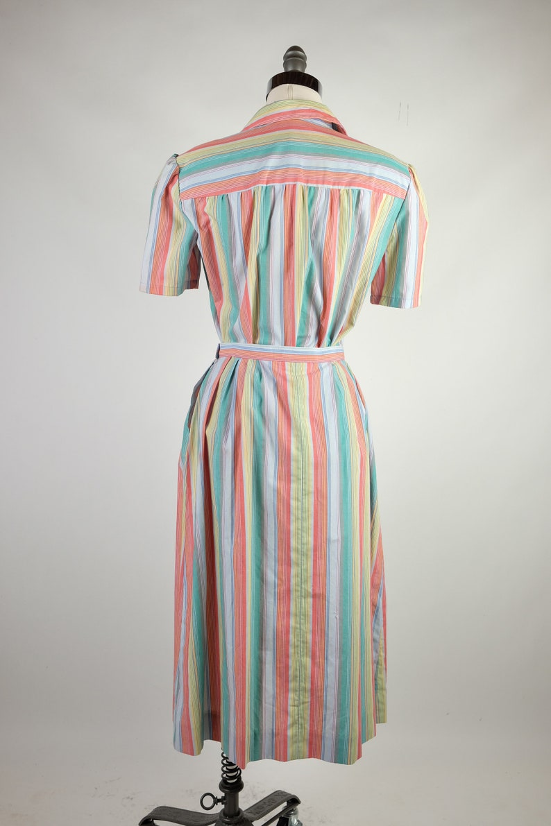 May include: A long, striped dress with a pink, yellow, blue, and green color scheme. The dress has a short sleeve and a belt.