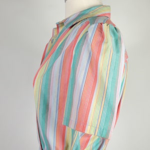 May include: A striped dress with a light blue, pink, green, and yellow color scheme. The dress has a button-up front and a short sleeve with a puff shoulder detail. The dress has a belt.