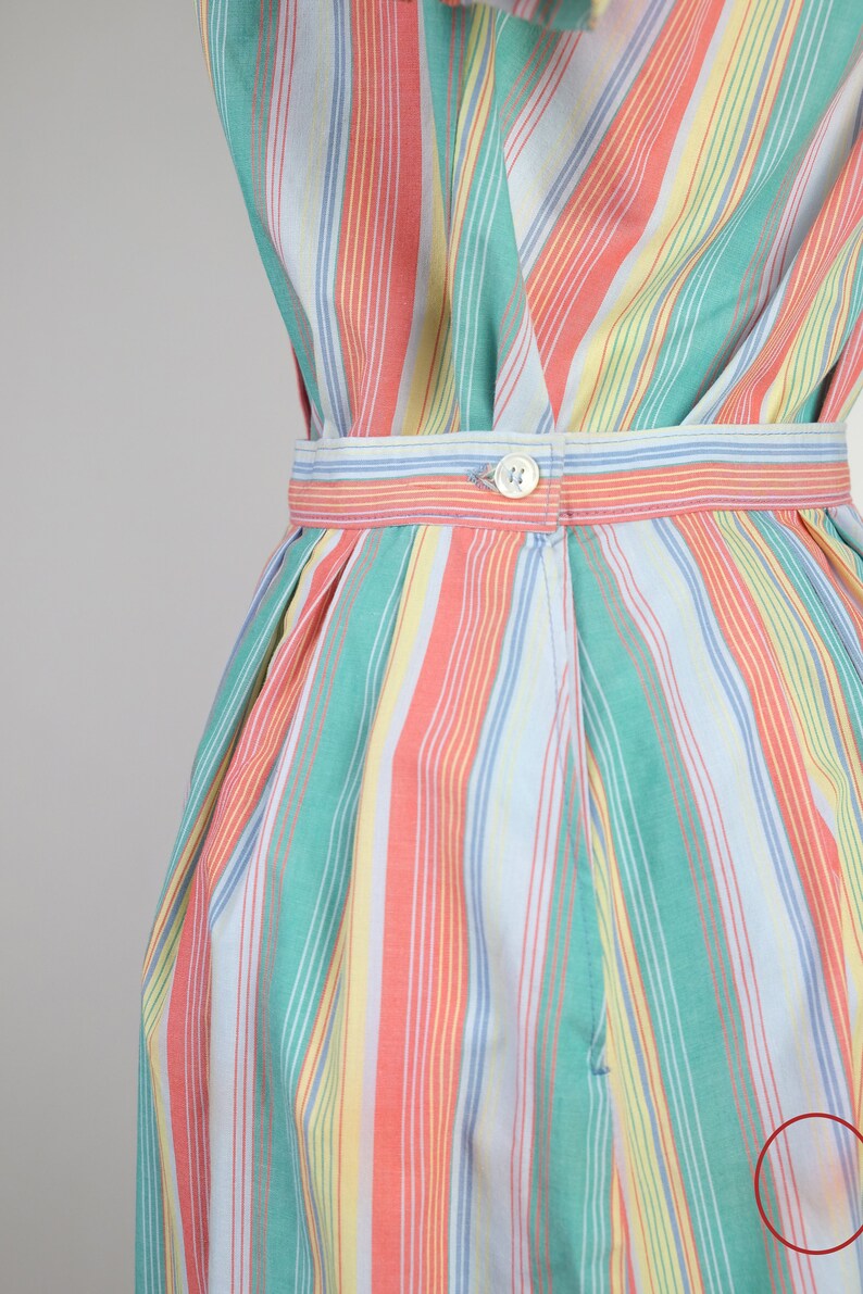 May include: A striped skirt with a blue, green, yellow, and pink color scheme. The skirt has a button closure and a pleated design.