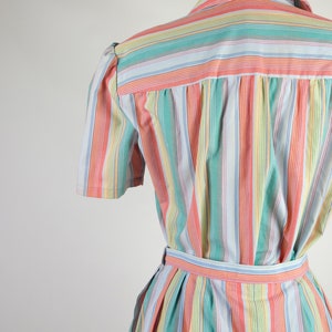 May include: A striped dress with a light blue background and colorful stripes in pink, green, and yellow. The dress has a short sleeve and a belt.