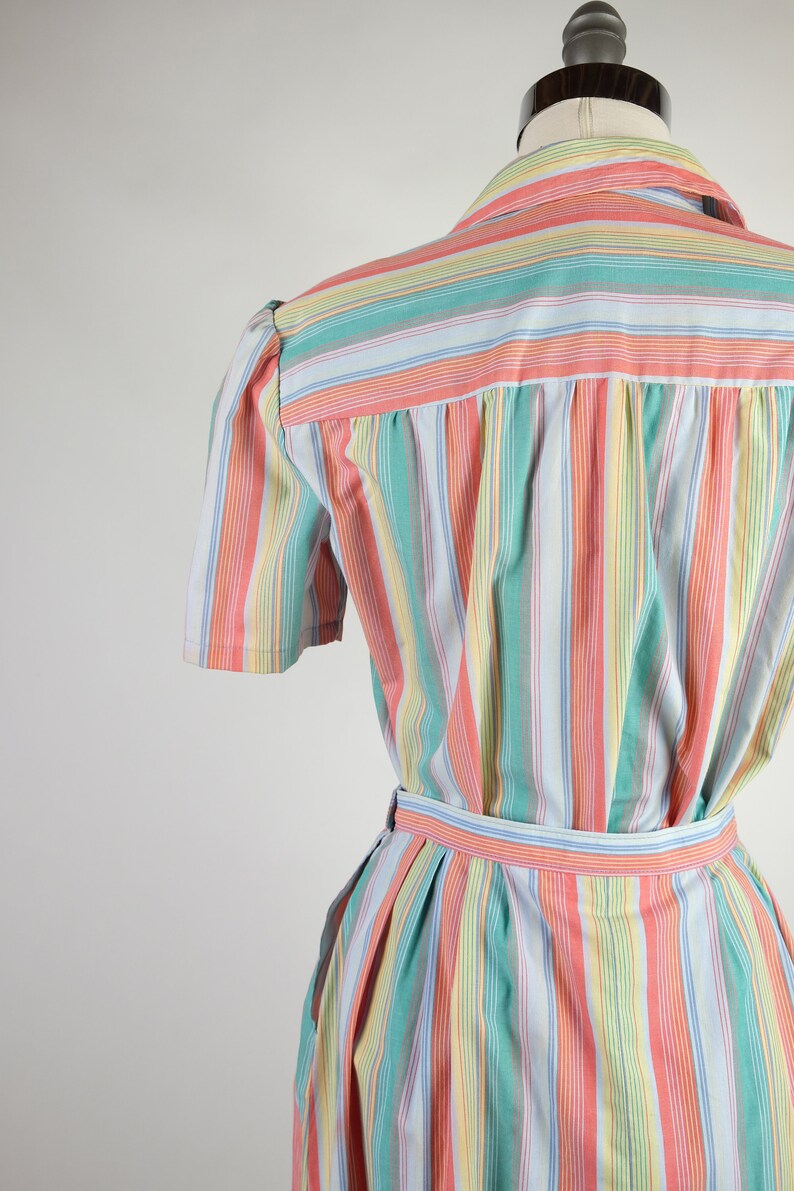 May include: A striped dress with a light blue background and colorful stripes in pink, green, and yellow. The dress has a short sleeve and a belt.