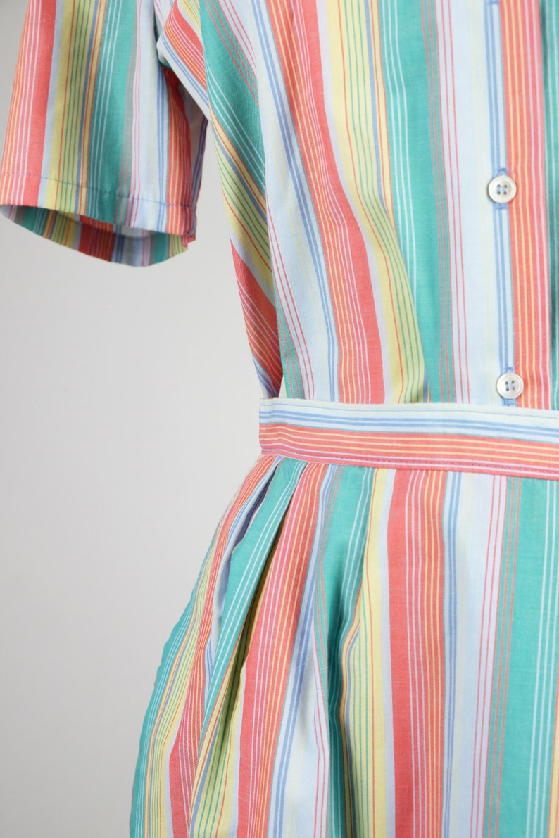 May include: A striped dress with a blue, green, yellow, and pink color scheme. The dress has a button-up front and a gathered skirt.
