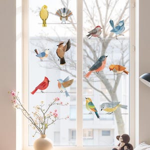 May include: A window is adorned with a series of decorative bird stickers. The birds, in diverse colours and patterns, are positioned on thin, horizontal lines. A vase of flowers on the windowsill complements the avian theme, adding a touch of nature to the room.