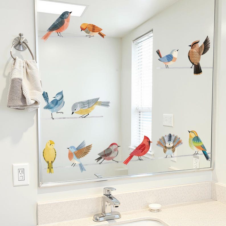 May include: A bathroom mirror decorated with colorful bird decals. The birds are perched on thin, horizontal lines, and feature various colors like red, blue, yellow, and orange. The mirror is above a white countertop with a chrome faucet and a small soap dish.