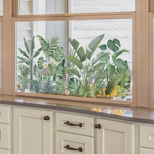 Peut inclure: Une fenêtre ornée d'un autocollant de plantes tropicales, présentant diverses feuilles vertes et quelques fleurs jaunes. L'autocollant est appliqué sur la fenêtre, créant une scène naturelle et vibrante. La fenêtre est encadrée en marron clair.