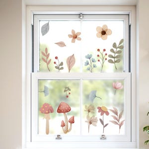 Könnte beinhalten: Ein weißes Fenster mit dekorativen Blumen- und Pilzaufklebern. Die Aufkleber zeigen verschiedene Blumen, Blätter und Pilze in sanften Pastellfarben wie Rosa, Beige und Hellblau, wodurch ein skurriles, von der Natur inspiriertes Design entsteht.