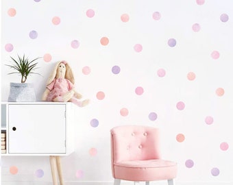 May include: A white wall decorated with pink, purple and peach watercolour polka dots. A pink armchair and a white dresser are in the foreground.