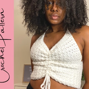 May include: A white crochet halter top with a gathered detail at the front. The top is worn by a person with curly hair.