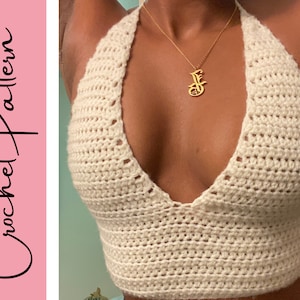 Könnte beinhalten: Ein weißes Häkel-Halter-Top mit tiefem V-Ausschnitt. Das Top ist mit einem einfachen Stichmuster gearbeitet und hat eine lockere Passform.