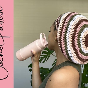 May include: A crocheted beanie in shades of brown, pink, and green. The beanie has a striped pattern and is being worn by a person.