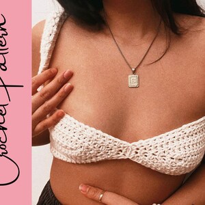 May include: White crochet crop top with a delicate, intricate stitch pattern. The top has a low-cut neckline and thin straps.