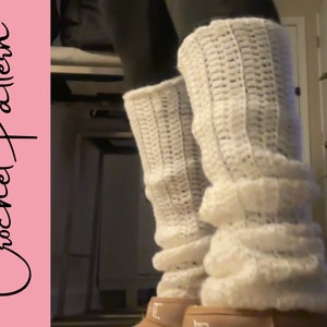May include: Cream-colored crochet leg warmers with a textured pattern. The leg warmers are worn over black leggings and brown boots. The text "Crochet Pattern" is on a pink background.