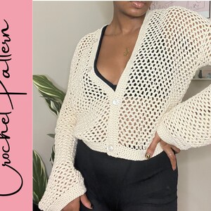 May include: A white crochet cardigan with a button closure and long sleeves. The cardigan has a loose fit and a delicate openwork pattern.