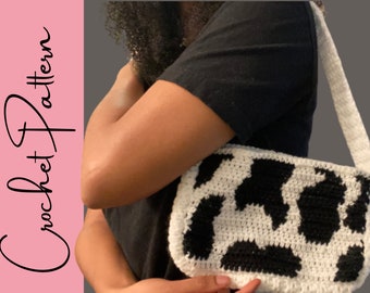 May include: A white and black crocheted handbag with a cow print design. The bag has a long strap and is worn over the shoulder.