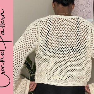 May include: A white crochet top with a loose fit and a large open stitch pattern. The top has long sleeves and a cropped length.