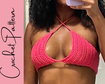Puede incluir: Un top halter de crochet rosa con un detalle de correa cruzada.