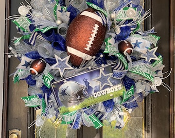 May include: A Dallas Cowboys themed wreath featuring a football, blue and green mesh, silver glitter, and a sign that reads "Cowboys".