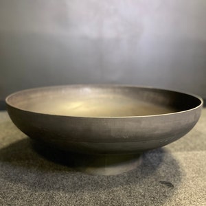 May include: A large, round, black metal fire pit bowl with a raised base. The bowl is empty and appears to be made of thick metal.
